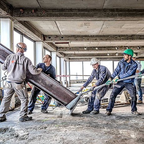 [Translate to Belgian French:] Des ouvriers du bâtiment tirent sur un poteau en acier.
