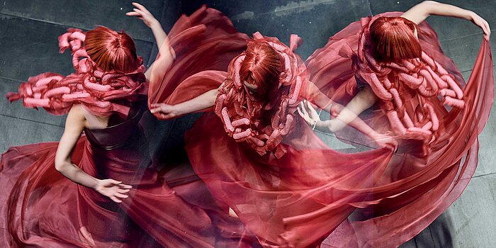 [Translate to Luxembourgish:] Tanzende Frau mit roten Haaren und rotem Kleid.